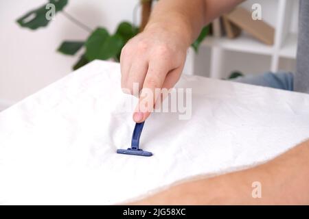 Ein Mann entfernt Stofftabletten mit einer Einweg-Rasiermaschine. Ein Rasiermesser zum Entfernen von Pellets. Stockfoto