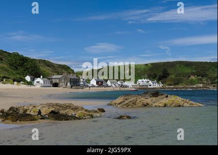 Blick über die Bucht bei Ebbe mit Felsen und klarem Wasser im Vordergrund, Pub und Häuser in der Ferne; klarer blauer Himmel an einem hellen Sommertag. Stockfoto