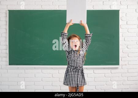 Aufgeregtes Kind in der Schule. Erstauntes Kind in der Klasse auf dem Hintergrund der Tafel. Bildung, Lernen und Kinderkonzept. Stockfoto