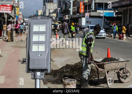 Nakuru, Kenia. 7.. Juli 2022. Ein Arbeiter wird dabei gesehen, wie er sich vorbereitet, eine solarbetriebene Straßenleuchte auf der Kenyatta Avenue im zentralen Geschäftsviertel zu installieren. Die Regierung von Nakuru County mit Unterstützung der Weltbank installiert Solar-Straßenlaternen, um die Sicherheit der Stadt zu verbessern. Die solare Straßenbeleuchtung ist umweltfreundlich, sie nutzt erneuerbare Energie aus der Sonne und trägt daher nur wenig CO2-Emissionen bei, die für den Klimawandel verantwortlich sind. (Bild: © James Wakibia/SOPA Images via ZUMA Press Wire) Stockfoto