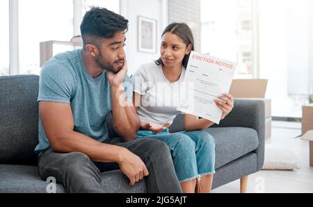 Ich dachte, Sie haben die Miete bezahlt. Aufnahme eines jungen Paares, das zu Hause auf dem Sofa sitzt und sich gestresst fühlt, nachdem er eine Räumungsanzeige erhalten hat. Stockfoto