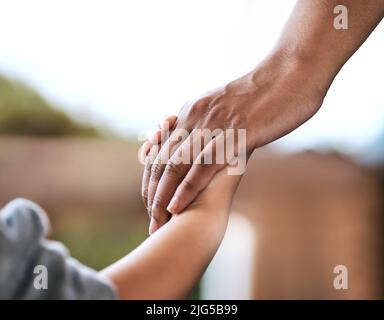Halte meine Hand fest. Aufnahme eines nicht erkennbaren Elternteils und Kindes, das die Hände zu Hause hält. Stockfoto