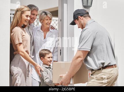 Hier ist Ihr Paket, Sir. Kurzer Schuss eines entzückenden kleinen Jungen, der die Lieferung seiner Familie von einem männlichen Kurier einsammelt. Stockfoto