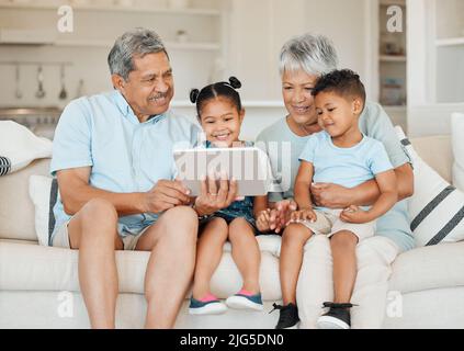 Familie ist keine wichtige Sache. Es ist alles. Aufnahme von Großeltern, die sich mit ihren Enkelkindern verbinden und ein digitales Tablet auf einem Sofa zu Hause verwenden. Stockfoto