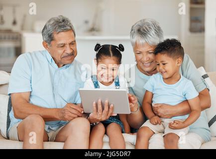 Die Erinnerungen, die wir mit unserer Familie machen, sind alles. Aufnahme von Großeltern, die sich mit ihren Enkelkindern verbinden und ein digitales Tablet auf einem Sofa zu Hause verwenden Stockfoto