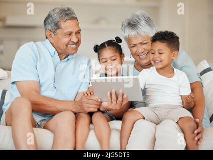 Familie ist Familie. Aufnahme von Großeltern, die sich mit ihren Enkelkindern verbinden und ein digitales Tablet auf einem Sofa zu Hause verwenden. Stockfoto