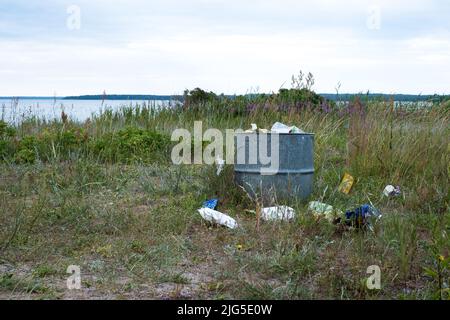 Überfüllte Mülltonne auf einer Wiese an sonnigen Sommertagen. Mülleimer in der Natur. Stockfoto