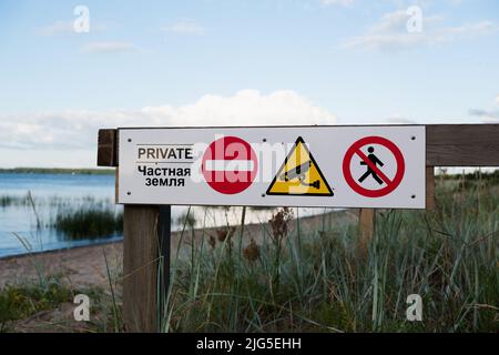 Ein 'Private Property'-Schild an einem Strand in Europa. Konzentrieren Sie sich auf Zeichen mit Logos. Entkochte Sandküste und Meer dahinter. Kein Zutritt, keine Umleitung Stockfoto