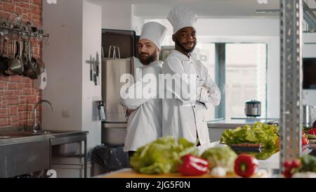 Porträt eines vielfältigen Teams, das in der professionellen Restaurantküche posiert und sich bereit macht, Gourmet-Gerichte zu kochen. Köche in Uniform machen Gericht Zubereitungen mit Lebensmittelzutaten für Gastronomie Rezept. Stockfoto