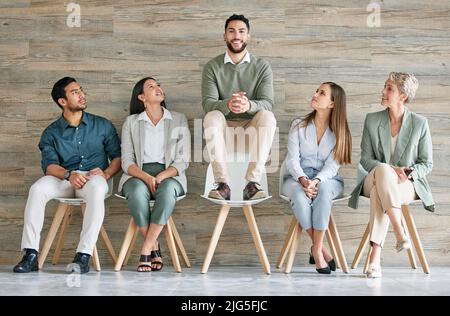 Seien Sie zuversichtlich genug, um sich von der Seite abzuheben. In voller Länge eine Gruppe von Geschäftsleuten, die in einer Reihe zusammen sitzen. Stockfoto
