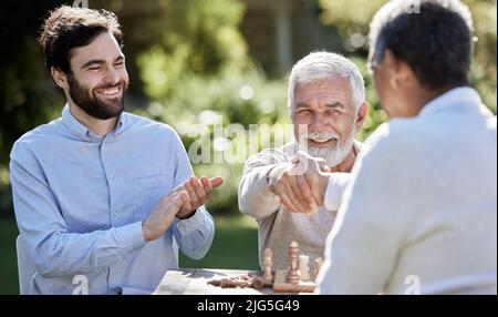 Freunde setzen den Partner in Schach Mate. Aufnahme einer Gruppe von Männern, die draußen eine Partie Schach spielen. Stockfoto