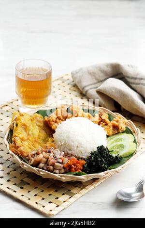 Nahaufnahme Nasi Campur Cumi Asine Surabaya, Weißer Reis mit sautiertem gesalzenem Tintenfisch, Sambal, Ei und gekochtem Cassava-Blatt. Stockfoto