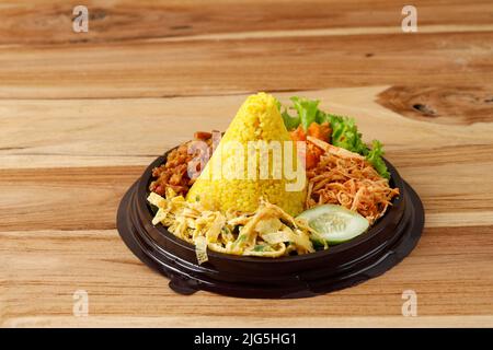 Mini-Tumpeng aus gelbem Reis mit einigen Beilagen, verzehrfertig, serviert zum Agustusan Indonesia Independence Day. Auf Holztisch Stockfoto