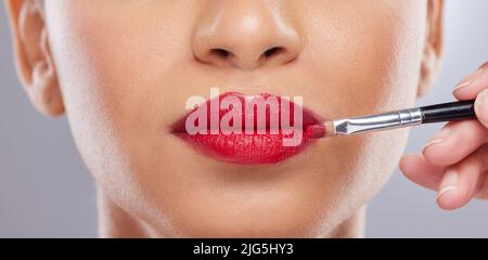 Ich habe alles über Perfektion. Ausgeschnittene Aufnahme einer nicht erkennbaren Frau, die im Studio posiert, während ein Make-up-Künstler Lippenstift aufträgt. Stockfoto