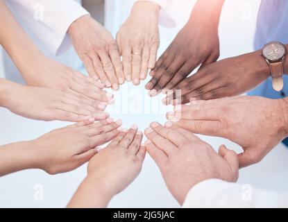 Wir können alles gemeinsam erreichen. Aufnahme einer Gruppe von nicht erkennbaren Ärzten, die bei der Arbeit ihre Hände zusammenstecken. Stockfoto