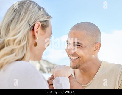 Ein junger Mann schlägt seiner Freundin im Sommer am Strand vor. Glückliches interrassisches Paar, das die Hände hält und lächelt. Bald Ehemann und Ehefrau werden Stockfoto