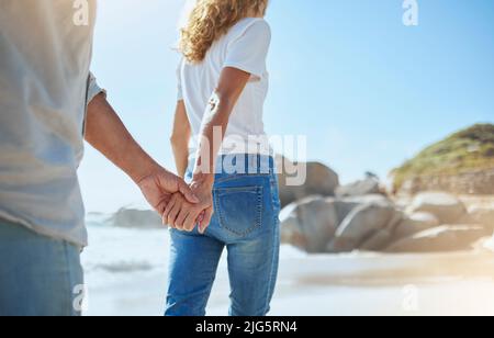 Nahaufnahme eines liebevollen reifen Paares, das sich im Sommer beim Strandspaziergängen die Hände hält. Liebevoll Ehemann und Ehefrau genießen Spaziergang am Meer während Stockfoto