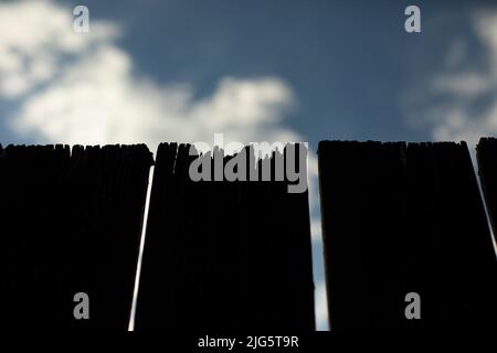 Nahaufnahme des Einzäunens der Platine. Gesprungene Zaunwand. Details der Landschaft. Einfacher dunkler Bretthintergrund. Stockfoto