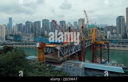 Dies ist Chongqing, China, wo eine Brücke über einen großen Fluss gebaut wird. Diese Brücke verbindet die beiden Seiten des Flusses und macht den Verkehr Stockfoto