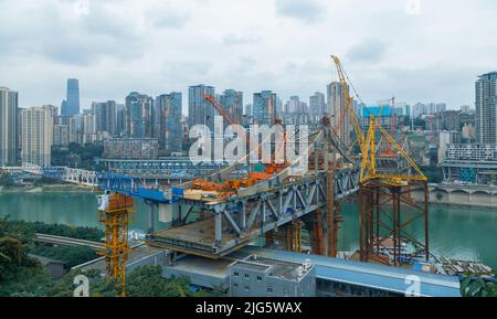 Dies ist Chongqing, China, wo eine Brücke über einen großen Fluss gebaut wird. Diese Brücke verbindet die beiden Seiten des Flusses und macht den Verkehr Stockfoto