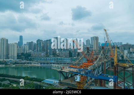 Dies ist Chongqing, China, wo eine Brücke über einen großen Fluss gebaut wird. Diese Brücke verbindet die beiden Seiten des Flusses und macht den Verkehr Stockfoto