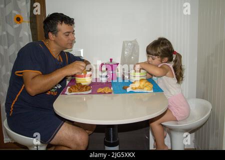 Bild eines jungen Vaters mit seiner Tochter, die noch immer zu lange beim Frühstück in Milch tauchte. Die richtige Motivation und Energie zu Stockfoto