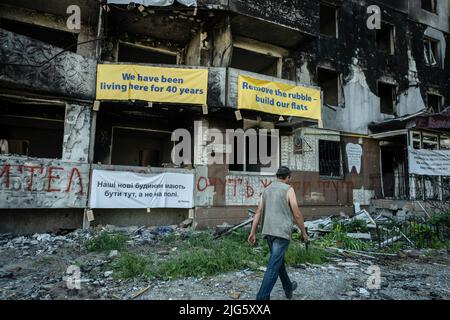 Ein Mann geht an den Ruinen eines zerstörten Wohnhauses in Borodyanka vorbei. Nach dem militärischen Versagen der Russen im Kyiv-Gebiet im März sind die einst leeren Städte nun voll von Bewohnern, die nach dem langen Krieg zurückkamen, um ihr Leben wieder aufzunehmen. Stockfoto