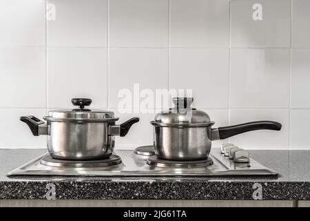 Ein paar rostfreie Töpfe auf dem Küchenherd mit Marmorplatte und weißer Fliesenwand Stockfoto