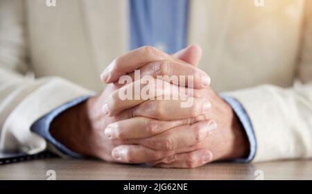 Selbstvertrauen muss in Ihrer Körpersprache offensichtlich sein. Ausgeschnittene Aufnahme eines nicht erkennbaren Geschäftsmannes, der allein in seinem Büro sitzt und die Hände zusammenhält. Stockfoto