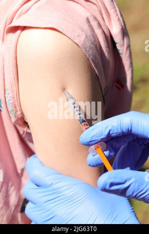 Arm des Mädchens während der Impfung gegen Viren und die Hände des Arztes mit blauen Plastikhandschuhen geschützt Stockfoto