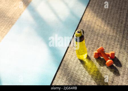 High-Angle-Ansicht der Wasserflasche und orange Hanteln durch blaue Übungsmatte auf Teppich, Kopierraum Stockfoto