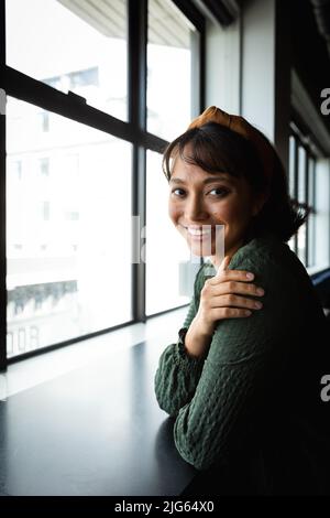 Porträt einer lächelnden jungen asiatischen Geschäftsfrau am Fenster im kreativen Büro Stockfoto