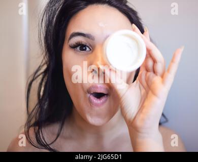 Ich kann es kaum erwarten, dieses neue Produkt auszuprobieren. Porträt einer schönen jungen Frau, die zu Hause Feuchtigkeitscreme auf ihre Haut anwendet. Stockfoto