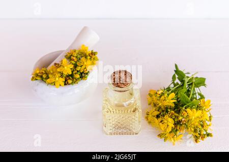 Glasflasche mit Korkverschluss mit natürlichem Johanniskraut-Öl. Mörser mit Blumen der Pflanze und Pistill. Das Konzept des Kochöls zu Hause Stockfoto