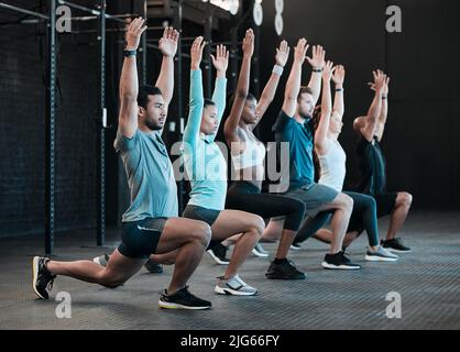 Mache einen Ausfallschritt, um die Beine zu verherrlichen. Aufnahme einer Gruppe von Leuten, die im Fitnessstudio zusammen Ausfallschritte machen. Stockfoto