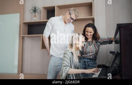 Glückliche Familie, Mutter, Vater und Tochter spielen zu Hause Klavier, Konzept für Familienbeziehung. Stockfoto