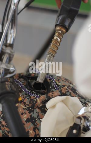 Fahrradtank an der Tankstelle auftanken. Konzept für die Verwendung fossiler Brennstoffe (Benzin, Diesel) in Verbrennungsmotoren, Nahaufnahme von Fahrradtank und Patrouillenpumpendüse Stockfoto