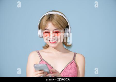 Optimistisch positive asiatische Mädchen genießt jedes bisschen Musik trägt Stereo-Kopfhörer auf ihren Ohren hält ein Mobiltelefon hört Lieblings-Audio-Track Stockfoto