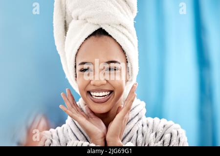 Ich liebe mein neues Hautpflegeregime. Eine kurze Aufnahme einer attraktiven jungen Frau, die zu Hause im Badezimmer ein Handtuch auf dem Kopf trägt. Stockfoto