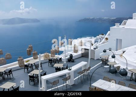 Santorini, Griechenland - 13. Mai 2021 : Blick auf eine malerische Terrasse mit Tischen, Stühlen und Lichtern, die an einem sonnigen Tag die Ägäis überblickt Stockfoto