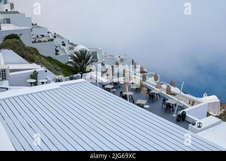 Santorini, Griechenland - 13. Mai 2021 : Blick auf eine malerische Terrasse mit Tischen, Stühlen und Lichtern, die an einem bewölkten Tag die Ägäis überblickt Stockfoto