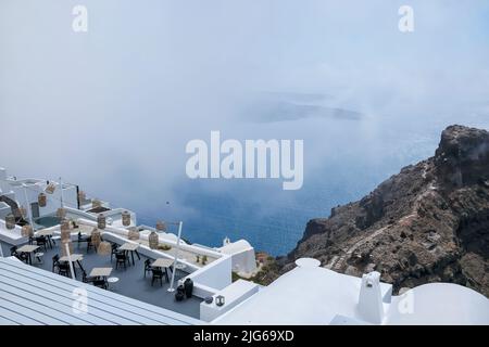 Santorini, Griechenland - 13. Mai 2021 : Blick auf eine malerische Terrasse mit Tischen, Stühlen und Lichtern, die an einem bewölkten Tag die Ägäis überblickt Stockfoto