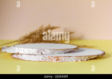 Ein leeres Holzpodium für Kosmetik und Parfums auf hellem Hintergrund mit trockenen Pflanzen Stockfoto