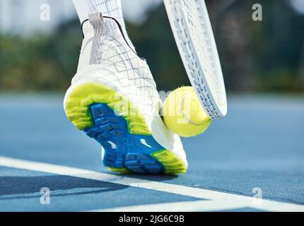 Nur Profis nehmen Tennisbälle auf diese Weise auf. Zugeschnittenes Bild eines nicht erkennbaren Mannes, der seinen Fuß und Schläger benutzte, um während des Schusses einen Tennisball abzuholen Stockfoto