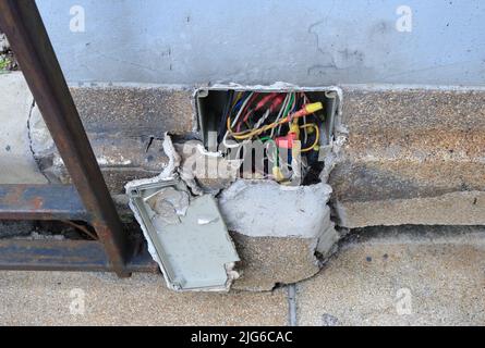Freiliegende elektrische Kabel in der Anschlussdose in der rissigen Wand, Weitwinkelansicht Stockfoto