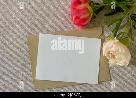 Das Layout einer Grußkarte oder Einladungskarte mit Pfingstrosenblumen auf einer grauen Tischdecke Stockfoto