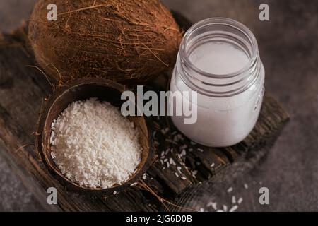 Kokosnuss, Flocken und Kokosöl im Glas auf dunklem Hintergrund Stockfoto