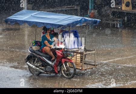 SAMUT PRAKAN, THAILAND, 28 2022. MÄRZ, Frau fährt bei starkem Regen ein Motorrad mit einem Wagen Stockfoto