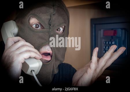 Ein Mann in einer Maske ruft den Assistenzdienst an, um Hilfe beim Öffnen eines verschlossenen Safes zu erhalten Stockfoto