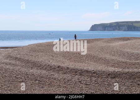 AXMOUTH, DEVON, ENGLAND - 12. 2020. JULI: Ein Mann und eine Frau gehen den Kiesspieß hinunter zum Meer in der Nähe von Axmouth Stockfoto